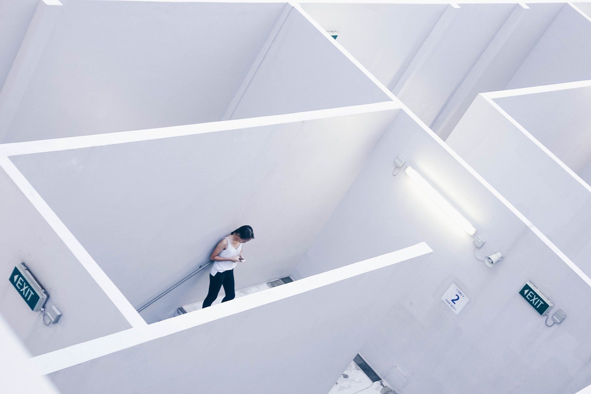 Person walking in a white maze, lit by fluorescent lights. Exit signs point the way.