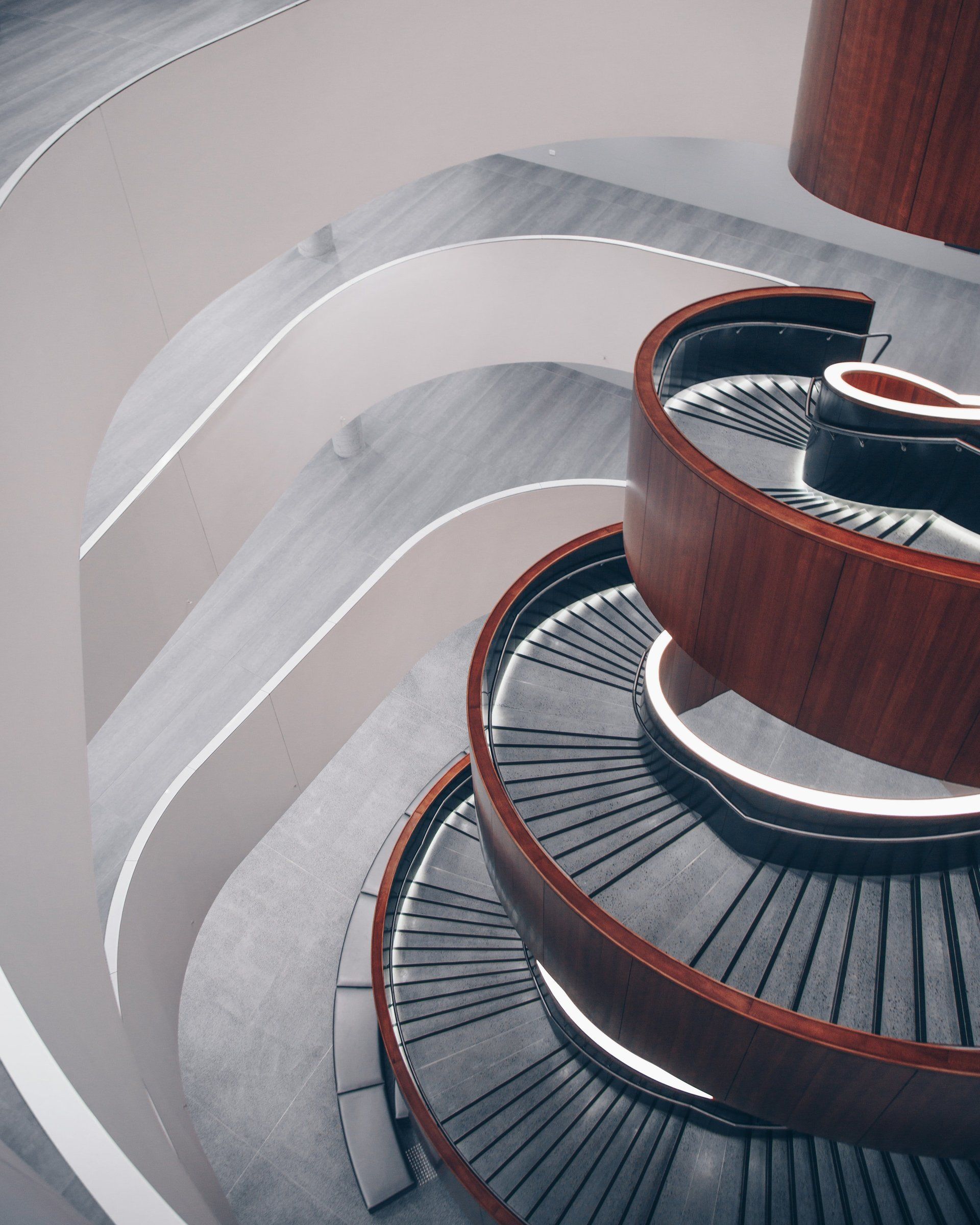 Spiral staircase with wooden railing and gray steps, viewed from above.