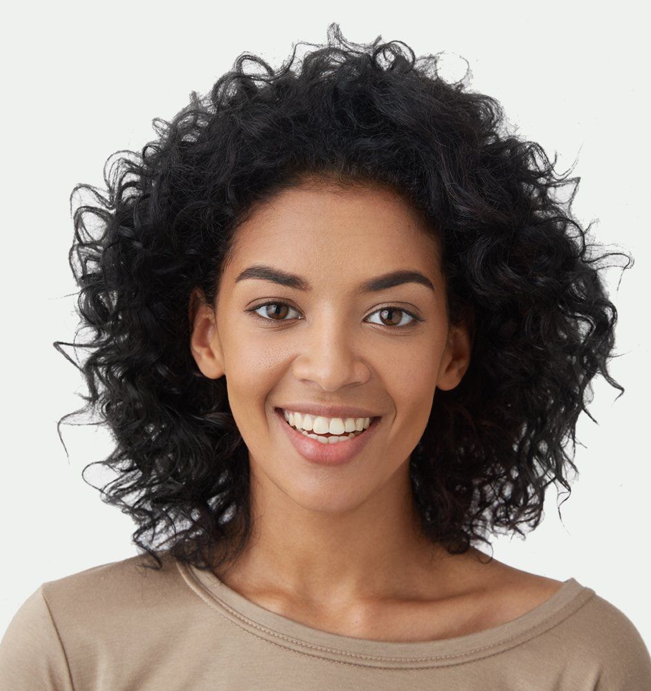 Woman with curly black hair smiles at the camera, wearing a beige top.
